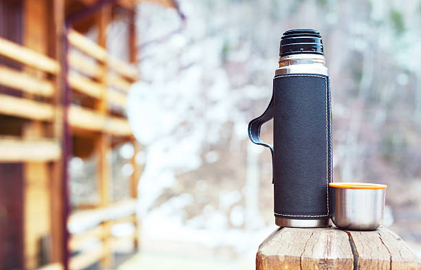 Steel thermos in black leather cover with a cup, outdoors
