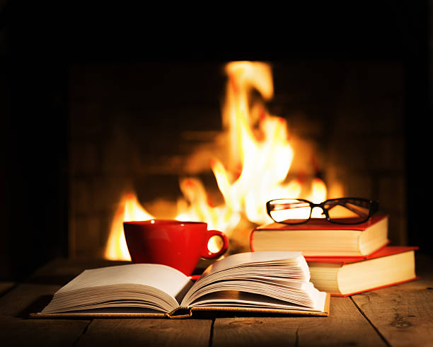 istock Red cup and old books on wooden table near fireplace. 523391996