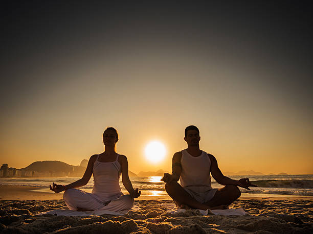 istock Couple meditating on the beach at sunset. 523395037
