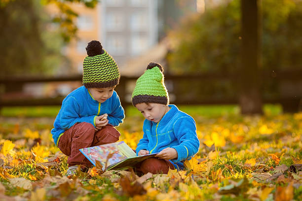 Two boys, reading a book on lawn in the afternoon