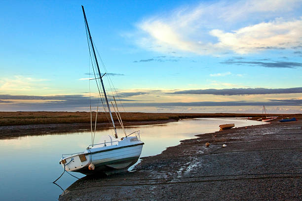 A late afternoon picture of sailing boats in calm water.  Grey clouds of an approaching storm are gathering over  the orange sky at sunset.