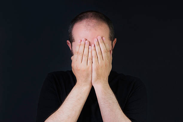 istock Man on black background, covering face with hands 523402946