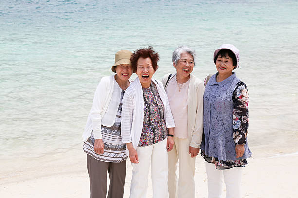 anziani donna in piedi sulla spiaggia - okinawa prefecture foto e immagini stock