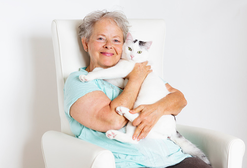 Happy senior woman, sitting in white chair and holding her white cat