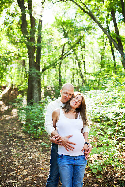 A husband is holding her pregnant wife while posing in a forest