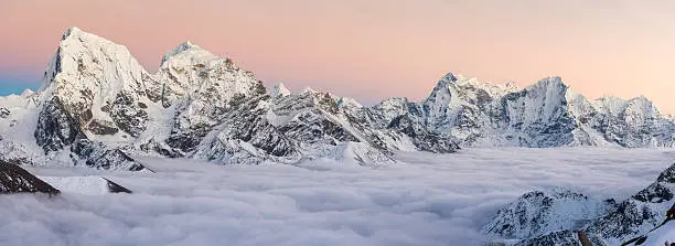 Delicate pink sunset skies above the snowy summits of Cholatse (6440m), Taboche (6542m), Kangtega (6752m) and Thamserku (6623m) rising through the clouds covering the Ngozumpa glacier and Gokyo deep in the high altitude Himalaya mountain wilderness of the Everest National Park on the Nepal Tibet border, a UNESCO World Heritage Site. ProPhoto RGB profile for maximum color fidelity and gamut.