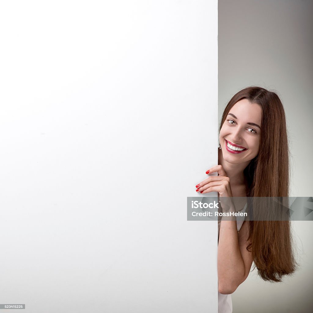 Woman pointing on white billboard over grey background in studio Smiling woman pointing on white empty billboard over grey background in studio Adult Stock Photo