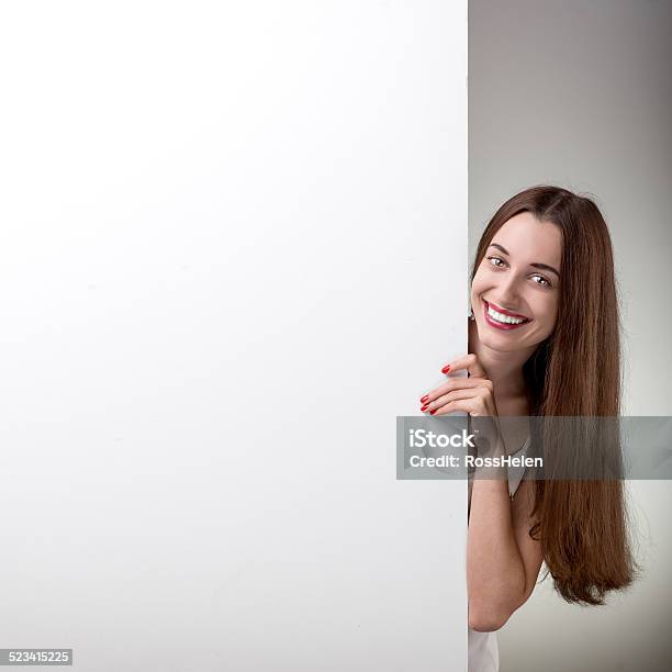 Woman Pointing On White Billboard Over Grey Background In Studio Stock Photo - Download Image Now