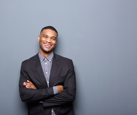 Portrait of a happy young business man smiling with arms crossed on gray background