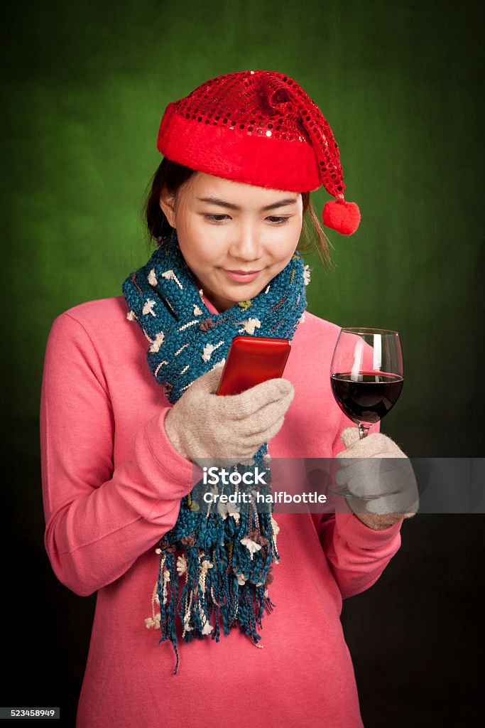 Asian girl with christmas hat ,wine and mobile phone Asian girl with christmas hat ,wine and mobile phone on dark green background Adult Stock Photo