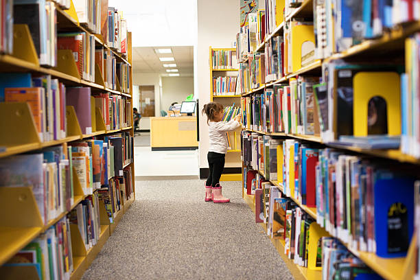little girl at the library picking a book - library stockfoto's en -beelden