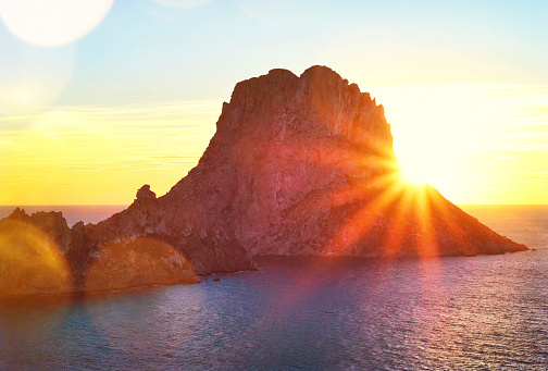 Sunset at Es Vedra, Ibiza Island. Sunbeam with lens flare behind the Isle of Es Vedra, magic rock of Ibiza.