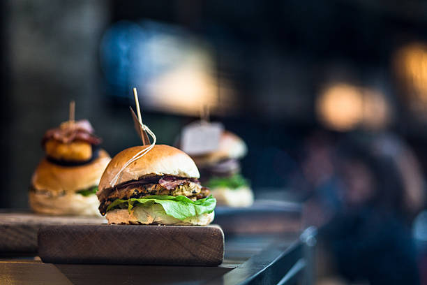 Close up image of a freshly flame grilled burger inside a bun, wilth lettuce, red onion, melted cheese and tomato. There are a few more burgers defocused in the background. The burger rests on a wooden board and the background is pleasantly defocused, leaving plenty of room for copy space. Horizontal colour image processed from an original RAW file,