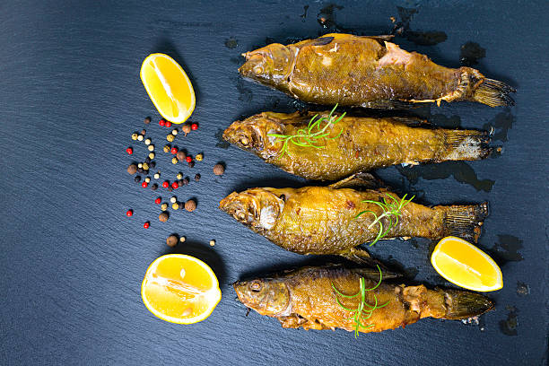top view of fried tench fish served with aromatic rosemary, top view of fried tench fish served with aromatic rosemary, lemon and dry peppers on slate background, close up tinca tinca stock pictures, royalty-free photos & images