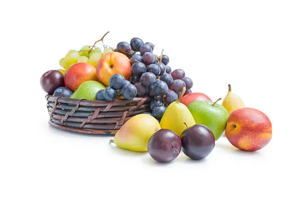 Mix of various fresh ripe fruits plums apples pears peaches and grapes  placed in a wicker basket and around isolated on a white background.