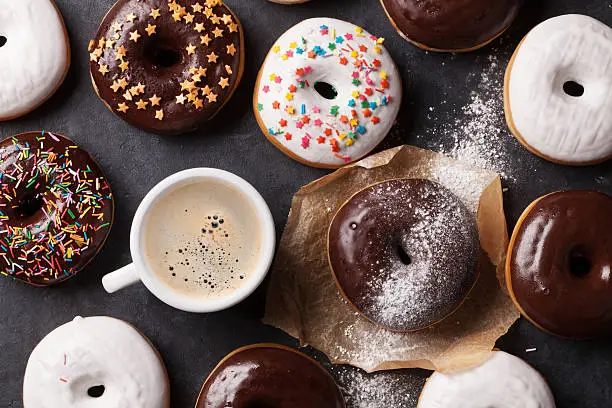 Colorful donuts and coffee on stone table. Top view