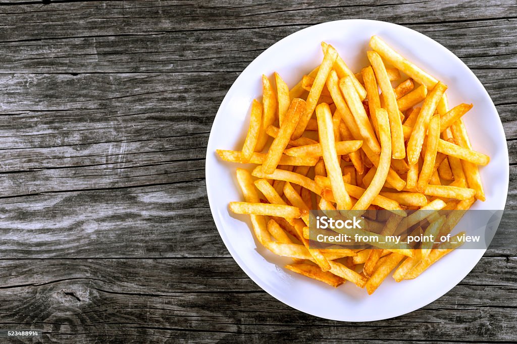 Tasty french fries on plate, on wooden table background Tasty french fries on white plate, on wooden table background, blank space left, top view French Fries Stock Photo