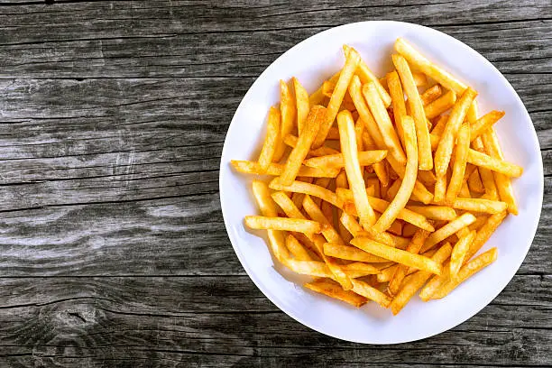 Tasty french fries on white plate, on wooden table background, blank space left, top view