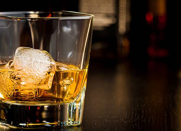 istock whiskey glass with ice in front of bottles 523489520