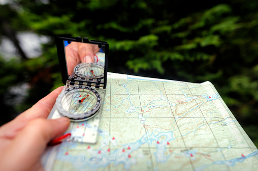 A close-up wide angle shot of a handheld map and compass being used in a backcountry wilderness situation.  Shot with a wide angle 20 mm lens the image shows the tool being used in the proper context.