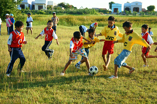 Binh Thuan, Viet Nam - October 25, 2014: Group of Asian kid playing football in team, Vietnamese little boy run on grass, outdoor activity of children physical education at countryside, Viet Nam, Oct 26, 2014