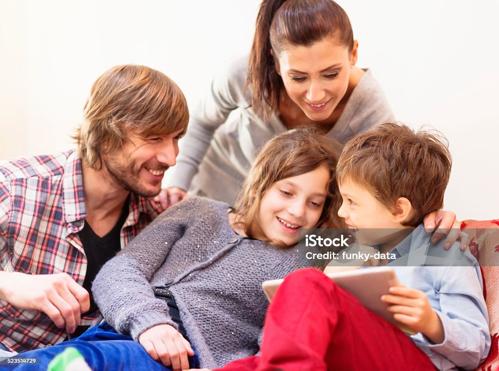 Young family with kids having fun with tablet computer Young parents with beautiful kids are enjoying a day on the sofa with a tablet computer. They are laughing and happy. Focus on the son. 25-29 Years Stock Photo