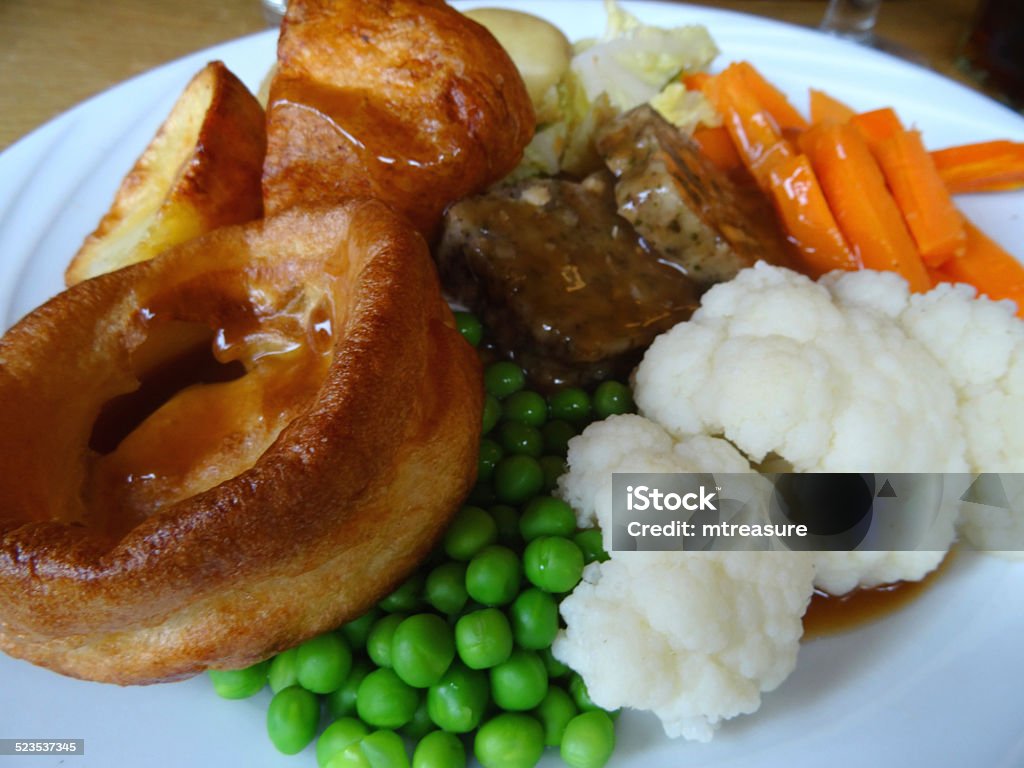 Sunday roast dinner, beef, Yorkshire pudding, gravy, roast potatoes, vegetables, cauliflower Photo showing a traditional Sunday roast dinner served up on a round white plate with a selection of seasonal vegetables and gravy.  The meal consists of roast beef with a Yorkshire pudding, cauliflower, sliced carrots (julienne style), shredded cabbage, stuffing and frozen peas / garden peas, as well as some boiled new potatoes and crunchy roast potatoes. Beef Stock Photo