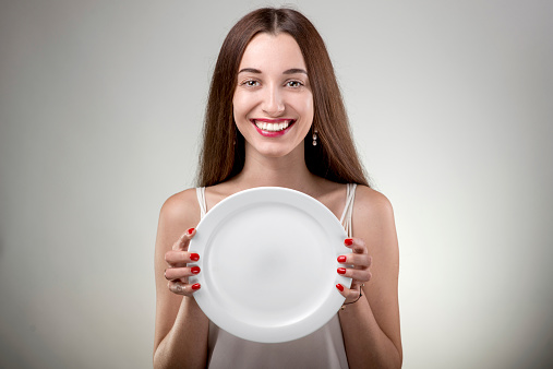 Young woman showing empty plate. Woman with plate in studio on white background
