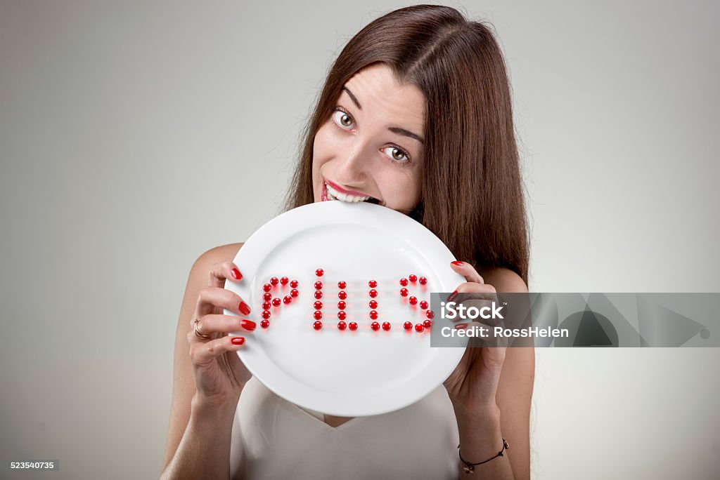 Young woman bites plate with pills Young woman bites plate with pills. Woman with plate and pills on it in studio on white background Adult Stock Photo