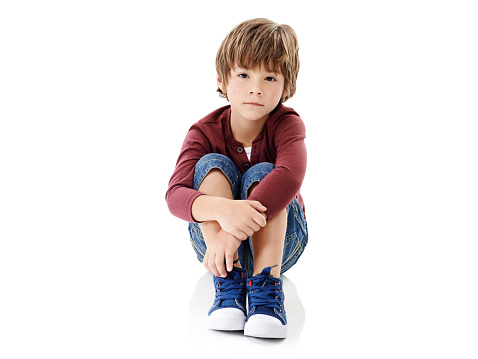 Studio shot of a cute little boy hugging his knees against a white background