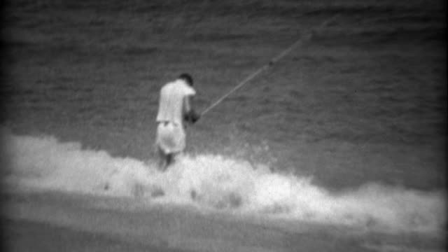 1936: Kid beach shore fishing on gulf bay waters with long pole.