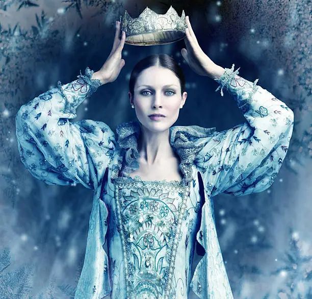 Shot of queen holding a crown over her head with snow falling around her