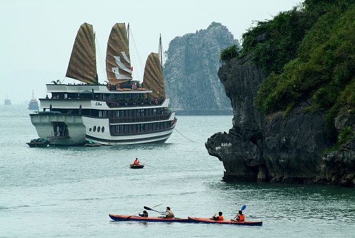 Quang Ninh,Vietnam-February 28,2014 : Tourist kayak paddle near large Junk ship overwhelmingly take tourist are typical in this region . More than 3,000 Islands are found in the area of Halong Bay in the Gulf of Tonkin on February 28,2014 in Halong Bay,Vietnam.
