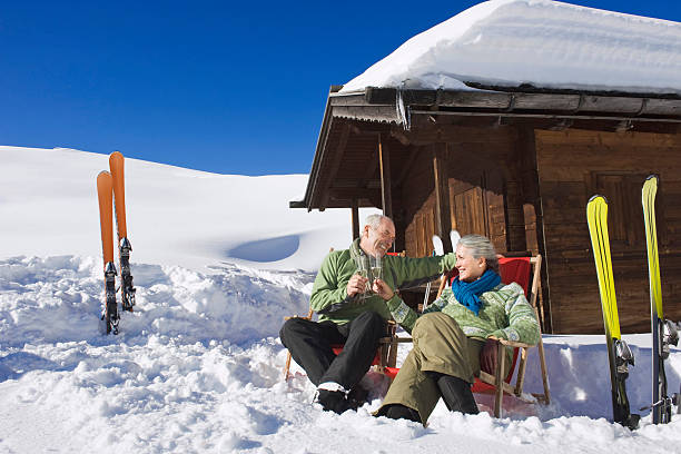 senior pareja en frente de log cabin, sosteniendo copas de champaña - skiing snow couple mountain fotografías e imágenes de stock