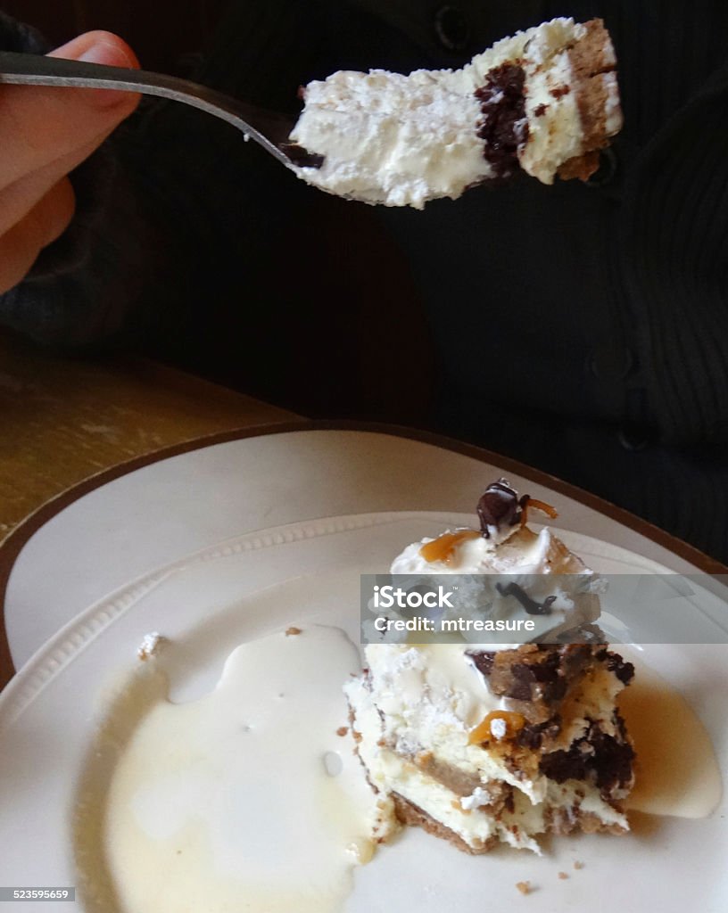 Eating homemade chocolate toffee fudge / caramel cheesecake, cake-slice, cream jug Photo showing a slice of rich homemade chocolate, toffee fudge and caramel cheesecake, which has been served on a round white plate with a small jug of single cream and is being eaten with a fork.  This indulgent cake has been topped with a thick layer of double cream icing, chocolate sauce and toffee sauce, and is being served at the end of a big Sunday roast dinner. Brown Stock Photo