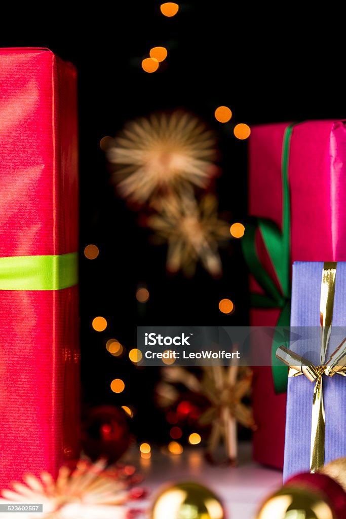 Gifts, glitters, spheres and stars. Crimson and blue gift boxes in focus in the mid-ground are giving way to the soft forms of festive spheres, straw stars and twinkles.. Blue Stock Photo