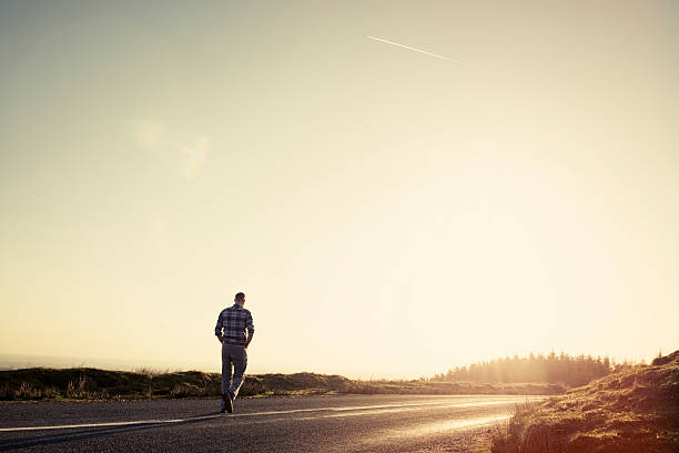 istock Man walking along an empty country road in afternoon sunshine 523614096