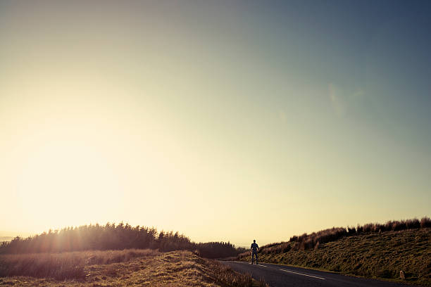 istock Man walking along an empty country road in afternoon sunshine 523614570