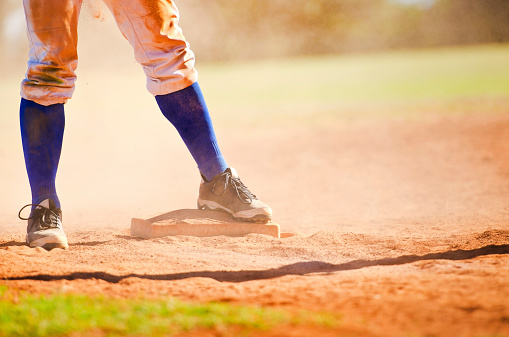 Baseball player wearing blue socks standing on a baseball base.