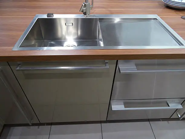 Photo showing a modern, stainless steel kitchen sink with a chrome mixer tap.  This single basin is pictured built into a real dark wood / walnut wooden worktop / block wood counter top.