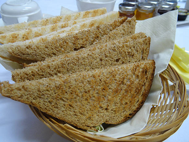 White and brown bread toast, wholemeal toast, breakfast wicker basket Photo showing a wicker basket at breakfast time, filled with slices of white and brown bread toast / wholemeal granary toast, being accompanied by some softened butter. granary toast stock pictures, royalty-free photos & images