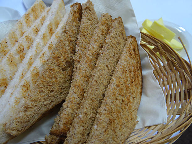 White and brown bread toast, wholemeal toast, breakfast wicker basket Photo showing a wicker basket at breakfast time, filled with slices of white and brown bread toast / wholemeal toast, being accompanied by some softened butter. granary toast stock pictures, royalty-free photos & images
