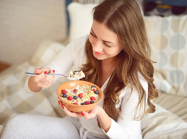 donna in pigiama in camera mangiare ai cereali e frutti di bosco - oatmeal porridge bowl spoon foto e immagini stock