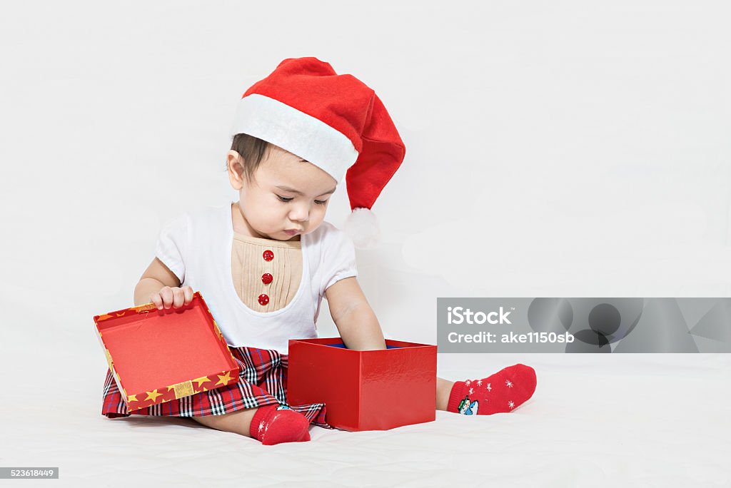 Asian baby with christmas cap pick up something Photo of curious and surprised asian baby in Santa cap looking at giftbox Adult Stock Photo