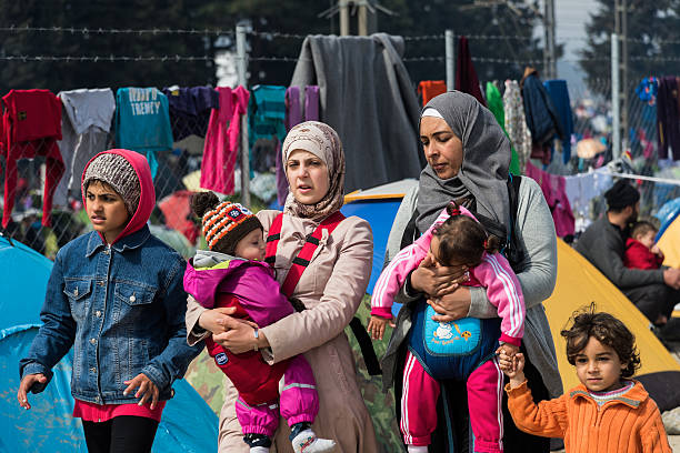 Women and children in refugee camp in Greece Eidomeni, Greece - March 17, 2016: Two women walk with their children in the refugee camp. refugee camp stock pictures, royalty-free photos & images