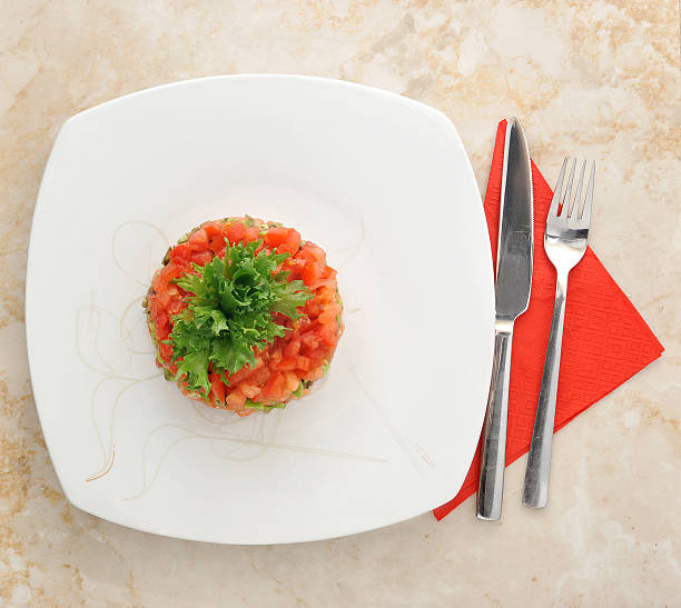 Tar-tar of salmon with salad leaves and red pepper on the plate. top view