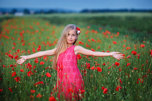 beautiful girl in red dress walks at poppy field.