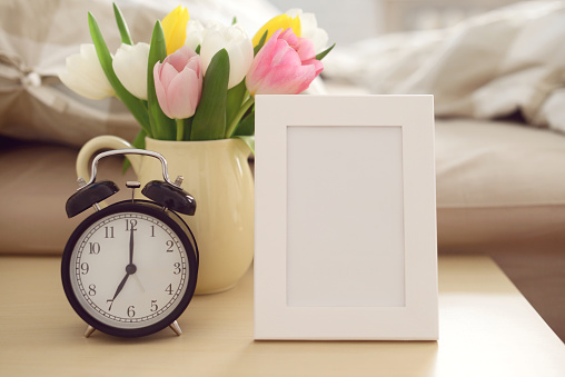 alarm clock,picture frame and a bouquet of tulips in a vase on the Night Table in the bedroom