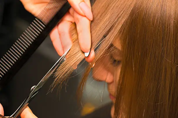 Female hair salon customer getting bangs trimmed.