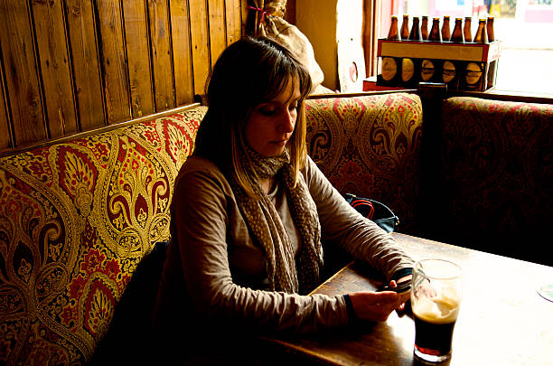 woman consults the mobil phone, while drinkinga pint of stout beer  in a pub in Ireland
